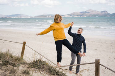 Lächelnder Mann hält die Hand einer Frau, die an einem Seil am Strand spazieren geht - JOSEF11424