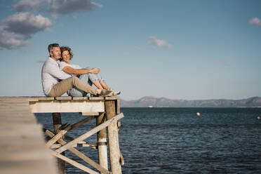 Lächelnde reife Frau mit Mann auf dem Steg sitzend an einem sonnigen Tag - JOSEF11427