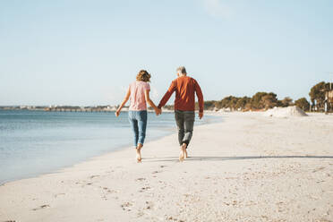 Couple holding hands walking on shore at beach - JOSEF11431