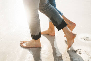 Mature man and woman walking barefoot on shore at beach - JOSEF11432