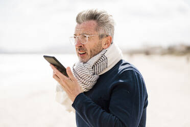 Älterer Mann mit Kopftuch, der am Strand mit seinem Handy telefoniert - JOSEF11455