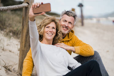 Glücklicher reifer Mann mit Frau nimmt Selfie durch Handy am Strand - JOSEF11467