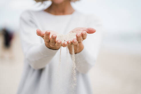 Die Hände einer reifen Frau halten Sand am Strand - JOSEF11468
