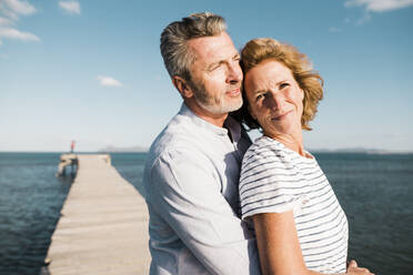 Smiling mature couple spending time with each other at jetty on sunny day - JOSEF11500