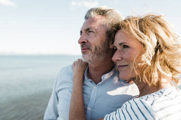 Lächelnde blonde Frau mit Mann am Strand stehend an einem sonnigen Tag - JOSEF11504