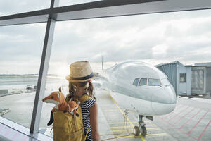 Girl with backpack watching airplane through glass window - RORF02975