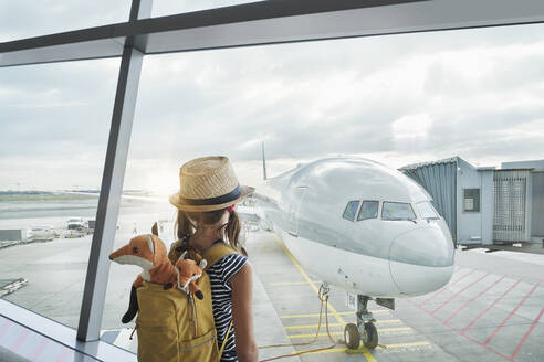 Girl with backpack watching airplane through glass window - RORF02975