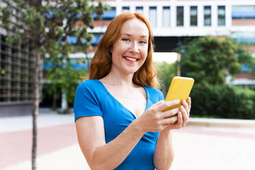 Lächelnde Frau mit Smartphone auf dem Fußweg - OIPF02099