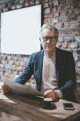 Confident senior businessman with newspaper in cafe - JOSEF11513