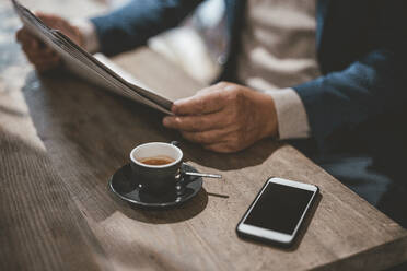 Businessman reading newspaper by coffee and smart phone at cafe - JOSEF11544