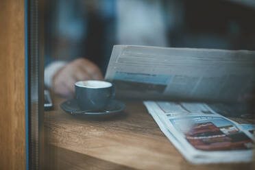 Geschäftsmann mit Zeitung und Kaffeetasse durch das Fenster eines Cafés gesehen - JOSEF11546