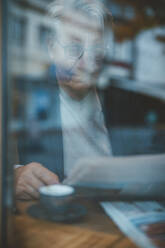 Businessman reading newspaper seen through window of cafe - JOSEF11547