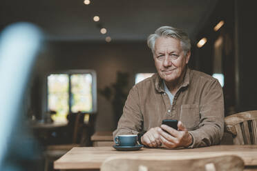 Smiling senior man with mobile phone in cafe - JOSEF11559
