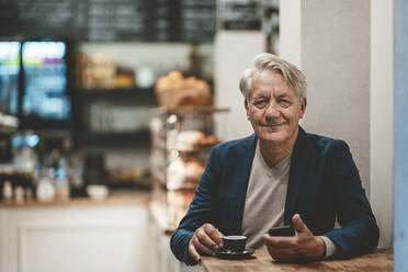 Smiling businessman with coffee on table in cafe - JOSEF11586
