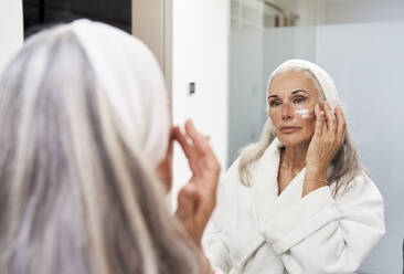 Ältere Frau trägt im Badezimmer Gesichtscreme auf - VEGF05757