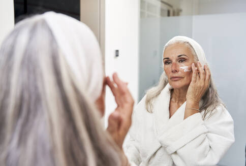 Mature woman applying face cream in bathroom - VEGF05757