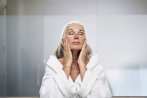 Woman with eyes closed touching face in bathroom - VEGF05760