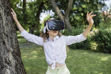 Mädchen mit Virtual-Reality-Simulator an einem Baum im Park - OSF00455