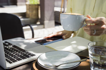 Hand eines Freiberuflers hält Kaffeetasse in einem Straßencafé - OSF00461