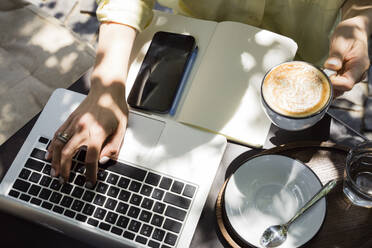 Freelancer with coffee cup using laptop at sidewalk cafe - OSF00462