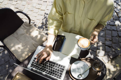 Freiberufler mit Kaffeetasse am Laptop sitzend in einem Straßencafé - OSF00463