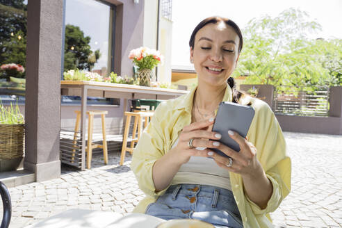 Lächelnde Frau mit Smartphone in einem Straßencafé - OSF00464