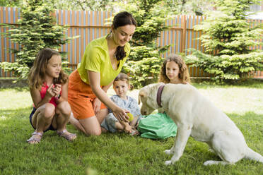 Smiling mother showing ball to dog by daughters at back yard - OSF00479