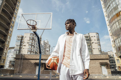 Junger Mann mit Basketball auf einem Sportplatz an einem sonnigen Tag - VPIF06862