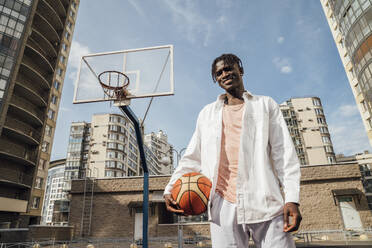 Smiling man young man standing with basketball at sports court - VPIF06863