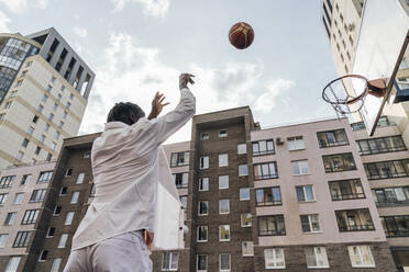Man throwing basketball in hoop in front of buildings - VPIF06869