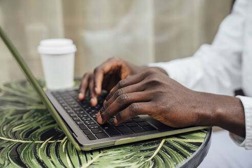 Hands of freelancer typing on laptop sitting at sidewalk cafe - VPIF06879
