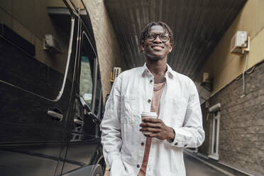 Lächelnder junger Mann mit Einweg-Kaffeebecher an einem Lieferwagen - VPIF06882