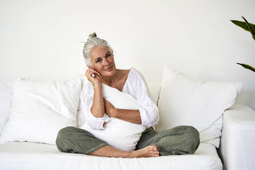 Smiling woman with cushion on sofa in living room - VEGF05787