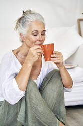Smiling woman smelling coffee in mug at home - VEGF05793