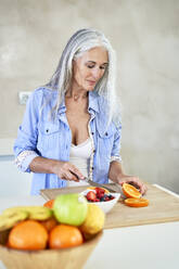 Mature woman cutting fruit at home - VEGF05804