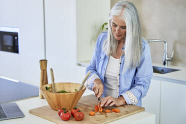 Woman with gray hair cutting carrots on kitchen counter - VEGF05806