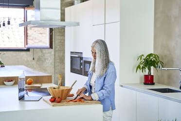 Mature woman cutting carrots on kitchen counter - VEGF05807