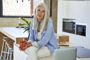 Ältere Frau mit Kaffeetasse auf dem Küchentisch sitzend - VEGF05810