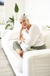 Smiling woman with cushion on couch in living room - VEGF05815