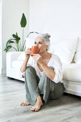 Mature woman drinking coffee sitting at home - VEGF05820