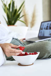 Woman holding strawberry using laptop at home - VEGF05825