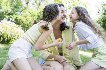 Happy mother getting kissed by daughters in park - OSF00499