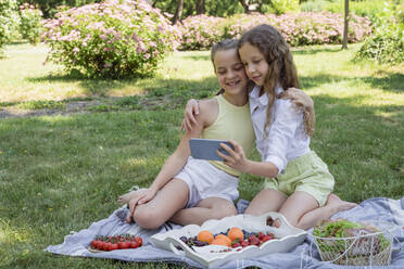 Smiling sisters taking selfie through smart phone in park - OSF00508