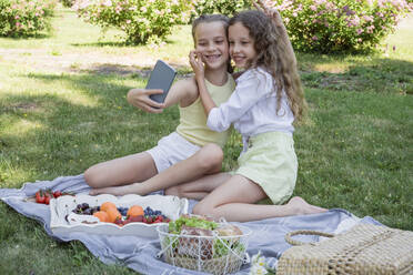 Girl pulling cheek of sister taking selfie at park - OSF00510