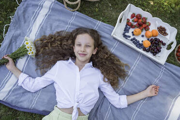 Lächelndes Mädchen mit ausgestreckten Armen auf einer Picknickdecke liegend - OSF00515