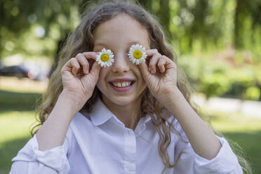 Glückliches Mädchen bedeckt Augen mit Blumen im Park - OSF00520