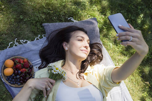 Lächelnde Frau nimmt Selfie durch Handy im Park - OSF00525
