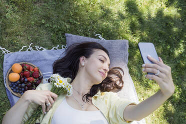 Lächelnde Frau, die ein Selfie über ein im Park liegendes Mobiltelefon macht - OSF00526