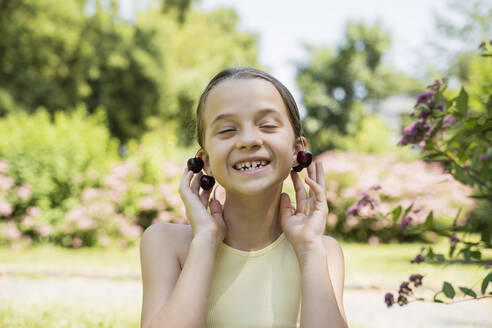 Lächelndes Mädchen trägt Kirschen als Ohrringe im Park - OSF00527