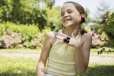 Playful girl wearing cherries as jewelry in park - OSF00528